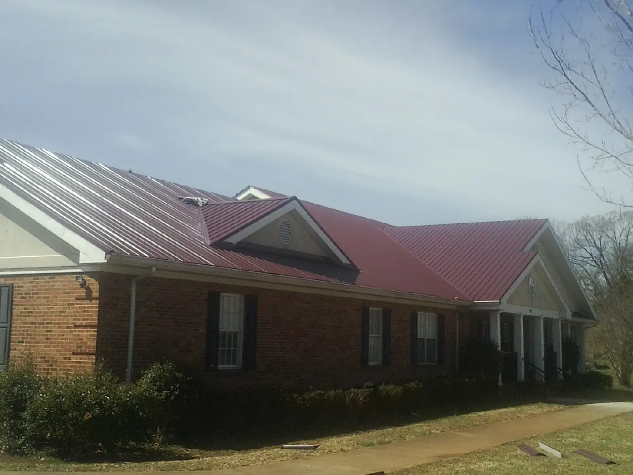 Red metal roof with gabled entries on a long brick building, from a Hail Damage Roof Repair job in Loa