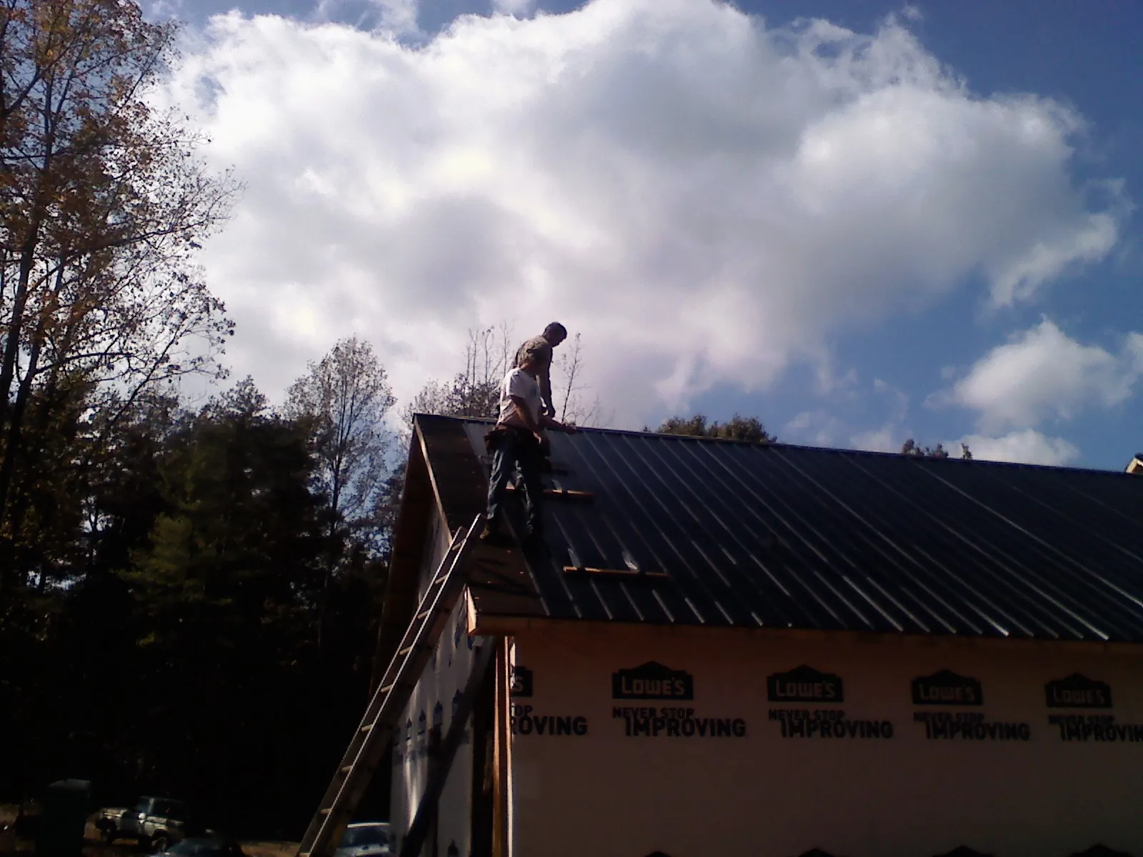 Roofer fastening dark metal panels high against a cloudy sky, from a Roof Inspection job in Loa